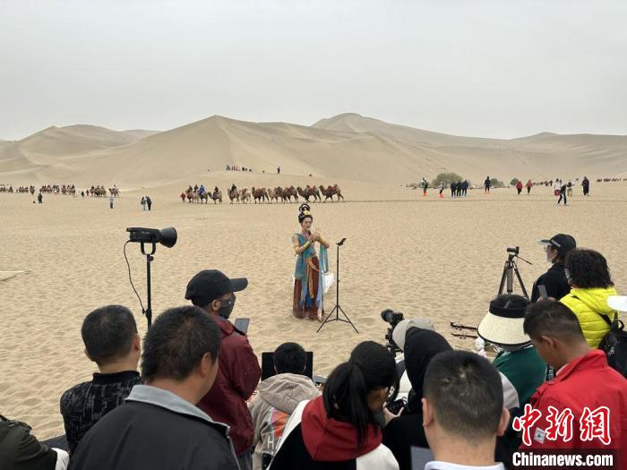 圖為2023年4月底，敦煌大漠“逐舞者”奧楠在鳴沙山月牙泉景區(qū)視頻直播，吸引游人圍觀?！●T志軍 攝